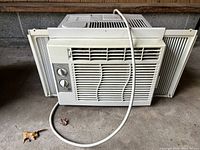 Front view of the beige window air conditioner unit showing control knobs, grille, and side panels.