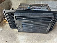 Front view of black Midea window air conditioner showing vent grille and control panel.