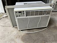 Front and side view of white window air conditioner unit showing grille, control panel, and side panels.