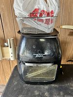 Front view of heavily used Power AirFryer Oven showing the black exterior, front handle, and glass door, with wire baskets and a flat pan placed on top.
