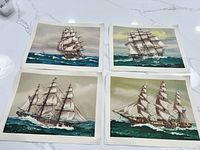 Four prints of American clipper ships laid flat on a white marble surface showing sailing scenes with large sails and rigging.