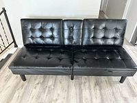 Front view of black leather futon sofa with button-tufted cushions and fold-down middle section.