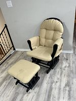Beige cushioned glider chair with matching stool, showing black wooden frames and visible stains on upholstery.