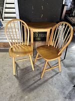 Full view of two wooden spindle back swivel chairs and the half-moon wooden hallway reading table placed against a black background.