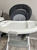 Front view of Graco high chair showing padded seat with grey striped fabric and white plastic tray with sections