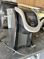 Photo of a black Keurig coffee maker with a clear water reservoir, showing signs of use but intact.