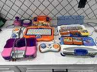Photo showing VTech VSmile Motion console, two joysticks, handheld gamepad, remote, foot pedal, and ten game cartridges on a kitchen counter