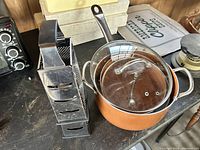 Two copper pots with glass lids and handles, shown side by side with two box cheese graters on a surface.