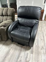 Black leather recliner with powered assist remote on right armrest, situated on wooden floor indoors next to a fabric recliner chair.
