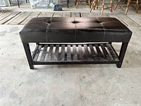 Angled front view of the rectangular brown leather bench showcasing its cushioned top and wooden lower shelf with slats.