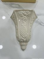 Front view of the cream-colored Lenox wall vase with embossed fruit designs including grapes and pineapple.