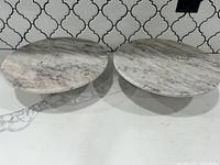 Two round marble cake or pie stands with white and grey veined tops, displayed side by side.