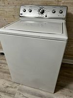 Front and side view of white Maytag top load washing machine showing metal control panel and lid.