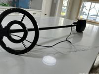 Side view of metal detector showing circular search coil and long shaft with cable running along it