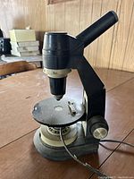 Side view of black and beige microscope showing stage, eyepiece, and focus knobs