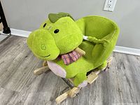 Full side angle view of green plush ride-on rocker dinosaur showing the wooden base and seat.