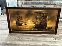 Frontal image of one ship oil painting with dark brown wooden frame and cream inner border, showing multiple ships in sunset color hues.