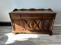 Front view of vintage wooden radio cabinet showing detailed carved top, front doors with X cross design, side louvered doors, and wood finish.
