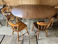 Photo of the oval vintage wooden dining table with four matching chairs in a garage setting, showing the table top and chair backs.