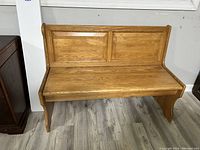 Front view of light-toned wood bench with two-paneled backrest and curved legs