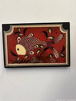 Front view of the signed laquered oil painting on board showing the stylized sardonic ocean fish on red background with decorative border.