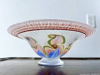 Side profile showing flared rim with pink concentric ring texture and pulled feather pattern inside the bowl.