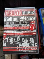 Front cover of Toronto Rocks concert DVD showing event title, artist lineup including Rolling Stones, AC/DC, Rush, Justin Timberlake, and others, with event details.
