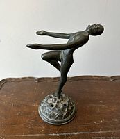 Front and side view of the statue showing the nude lady figure with arms extended forward on a circular base with holes.