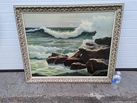 Full view of the vintage coastal tide art print in carved wood frame against plain background with water bottle for scale.
