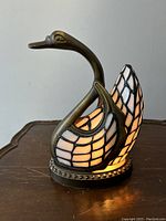Front view of lit swan lamp on wooden surface showing metal neck and stained glass wings