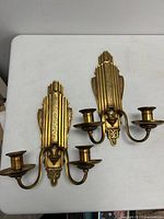 Pair of bronze patinated metal Art Deco wall sconces laid on table showing front design and candleholders.