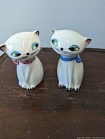 Front view of the pair of ceramic Siamese cat salt and pepper shakers, showing the pink and blue collars and painted facial details.