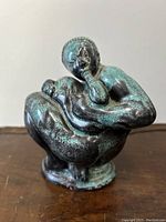 Front angle view of the sculpted pottery figurine showing the seated human figure with hands near face and textured glaze.