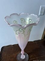 Top view showing the wavy ruffled rim and green/white feather pattern on pink background.