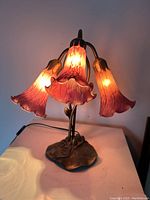 Front view, illuminated, showing three magenta glass shades and metal lily-pad base