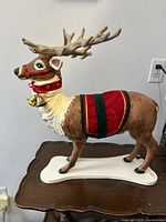 Side view of the full reindeer figure showing brown and white body, red collar with gold bells, and green/red harness on white base.