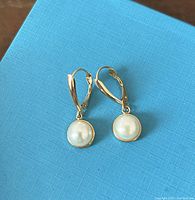 Pair of leverback earrings with white round pearls displayed on blue textured box.