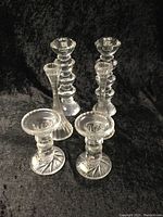 3 pairs of crystal and glass candle holders arranged on black fabric background showing different styles and heights.