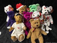 Nine assorted Beanie Babies bears of various colors and designs with Ty tags, displayed together against a black background.