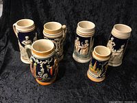Full view of the set of five ceramic German beer steins arranged on black background showing relief details and colors.