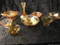 Eight assorted carnival glass pieces arranged on a black cloth, showing varied shapes and iridescent colors.