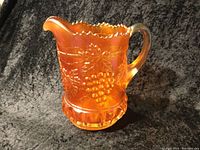 Front and side view of the carnival glass pitcher showing the grapevine embossed pattern and matte orange finish.