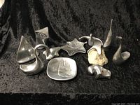 Nine assorted silver-tone metal art pieces of abstract and stylized organic shapes arranged on black velour fabric background.