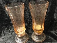 Two amber Depression glass candle holders side by side, showing their etched floral patterns and clear bases.
