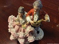 Full view of couple figurine depicting man playing mandolin and woman holding fan with ruffled attire.