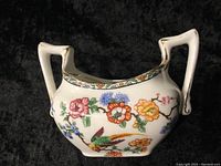 Image showing the front side of the bowl with floral and bird decorations and gold trim on handles.