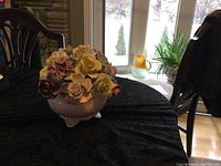 Flower bowl made of fine bone china with detailed ceramic flowers in multiple colors arranged in a bouquet, sitting on a table near a window.