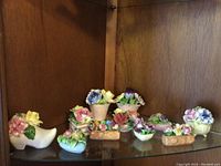 View of eleven assorted fine bone china flower arrangements on a glass shelf in a wooden corner display.