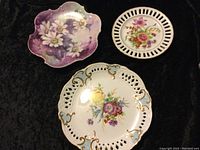 Three decorative fine bone china plates with floral designs on display against a dark background showing overall designs and shapes.