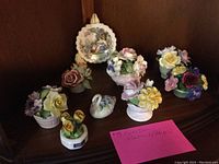 Photo showing eight fine china items including six flower arrangements, a decorative mini plate, and a small swan figurine, all displayed on a wood surface.